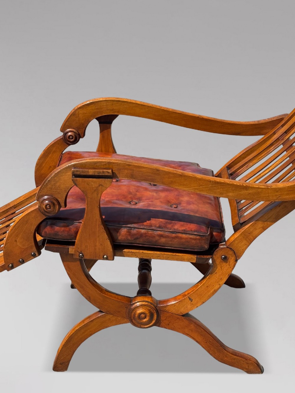 A pair of 19th-century Victorian walnut reclining armchairs featuring slatted backrests, extendable footrests, curved X-frame bases, and brown leather seat cushions. View XI