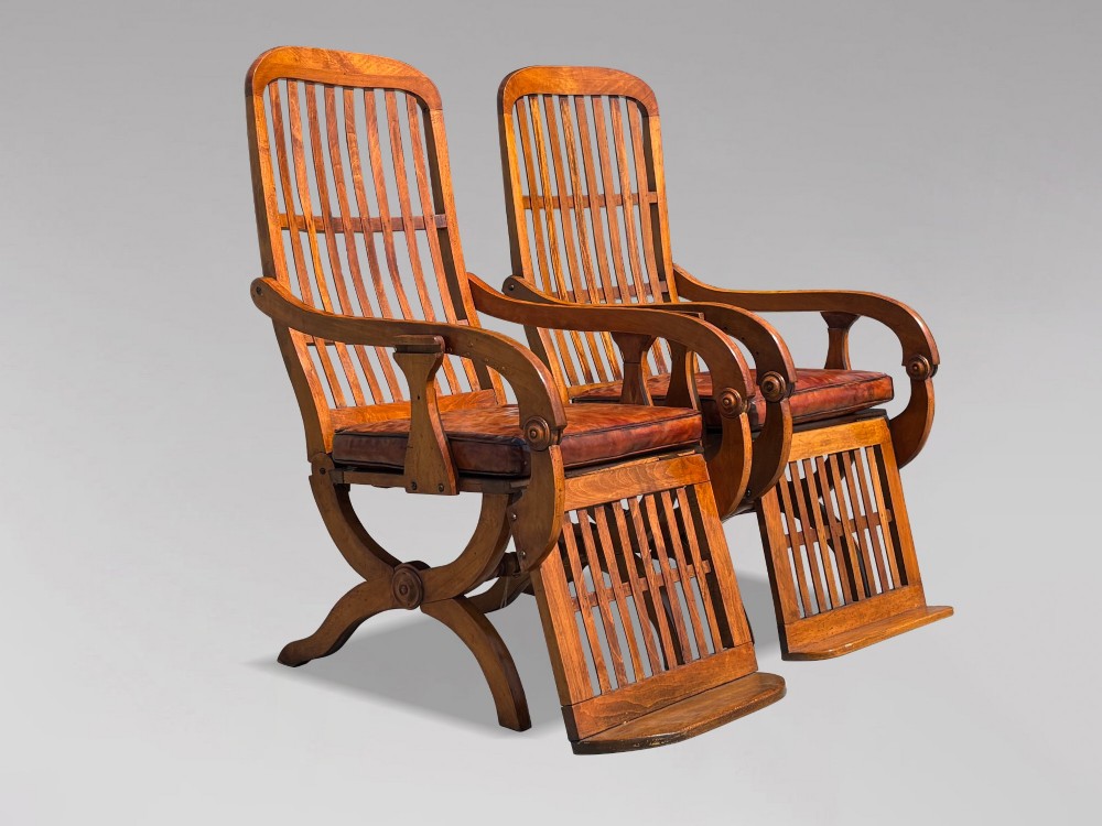 A pair of 19th-century Victorian walnut reclining armchairs featuring slatted backrests, extendable footrests, curved X-frame bases, and brown leather seat cushions. View XII