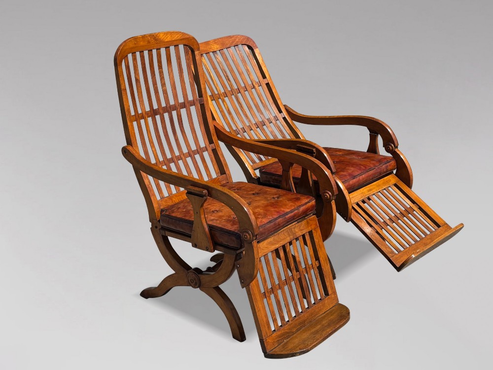 A pair of 19th-century Victorian walnut reclining armchairs featuring slatted backrests, extendable footrests, curved X-frame bases, and brown leather seat cushions. View XIV