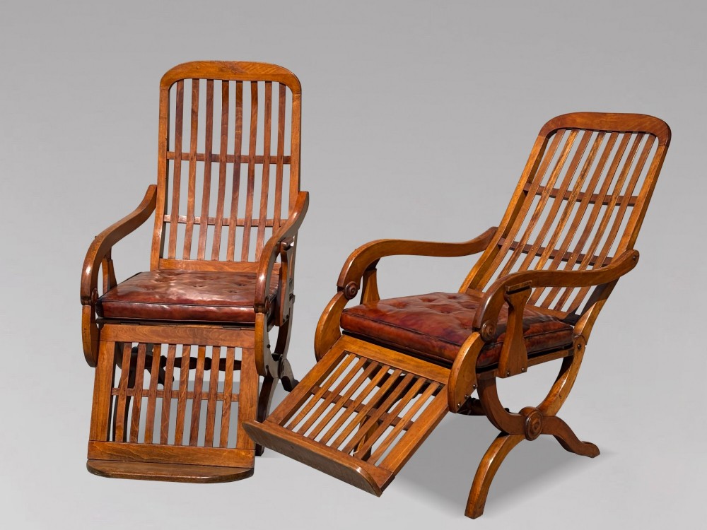 A pair of 19th-century Victorian walnut reclining armchairs featuring slatted backrests, extendable footrests, curved X-frame bases, and brown leather seat cushions. View XV
