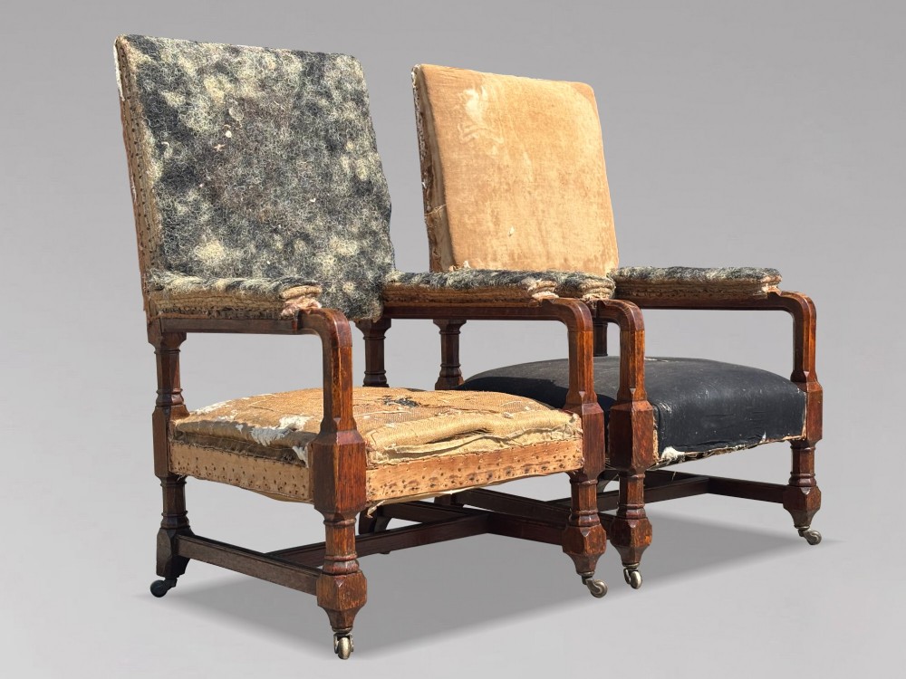 A pair of 19th-century Victorian oak Gothic Revival open armchairs featuring carved timber frames, turned legs with brass castors, and exposed upholstery padding. View II