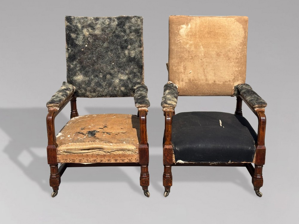 A pair of 19th-century Victorian oak Gothic Revival open armchairs featuring carved timber frames, turned legs with brass castors, and exposed upholstery padding. View III