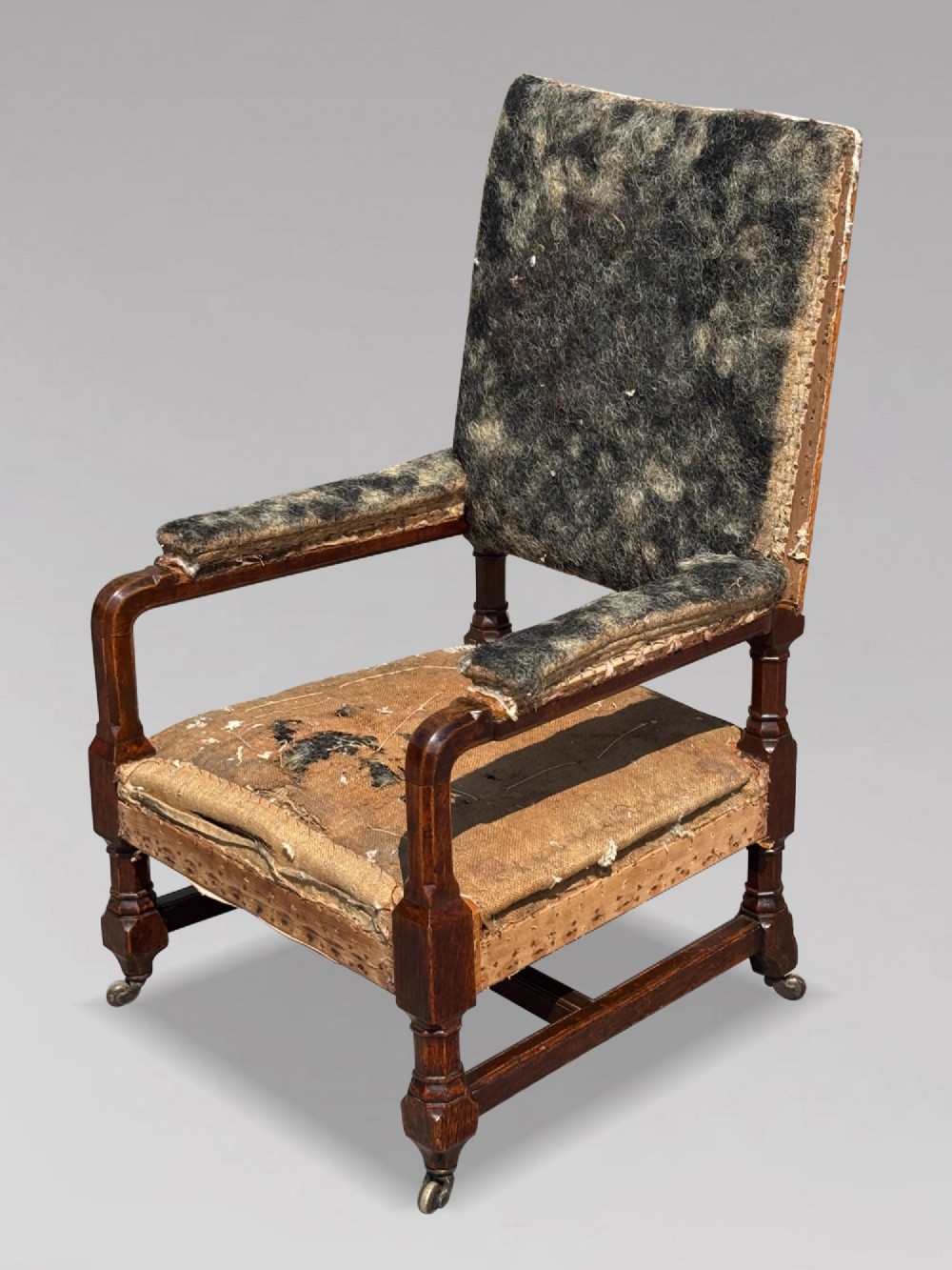 A pair of 19th-century Victorian oak Gothic Revival open armchairs featuring carved timber frames, turned legs with brass castors, and exposed upholstery padding. View IV