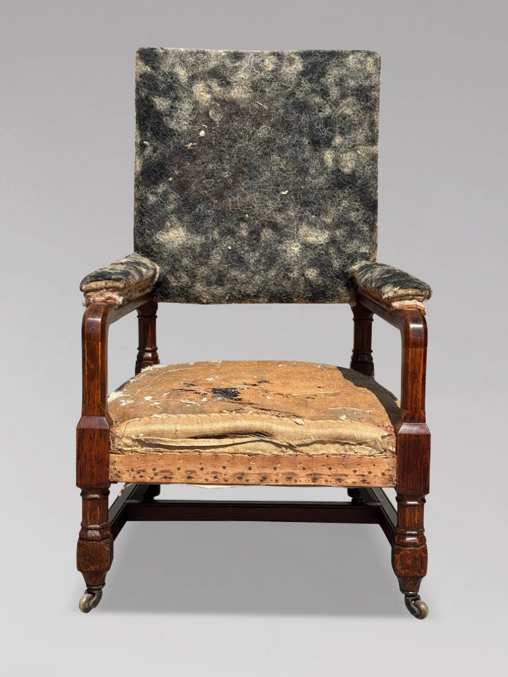 A pair of 19th-century Victorian oak Gothic Revival open armchairs featuring carved timber frames, turned legs with brass castors, and exposed upholstery padding. View V