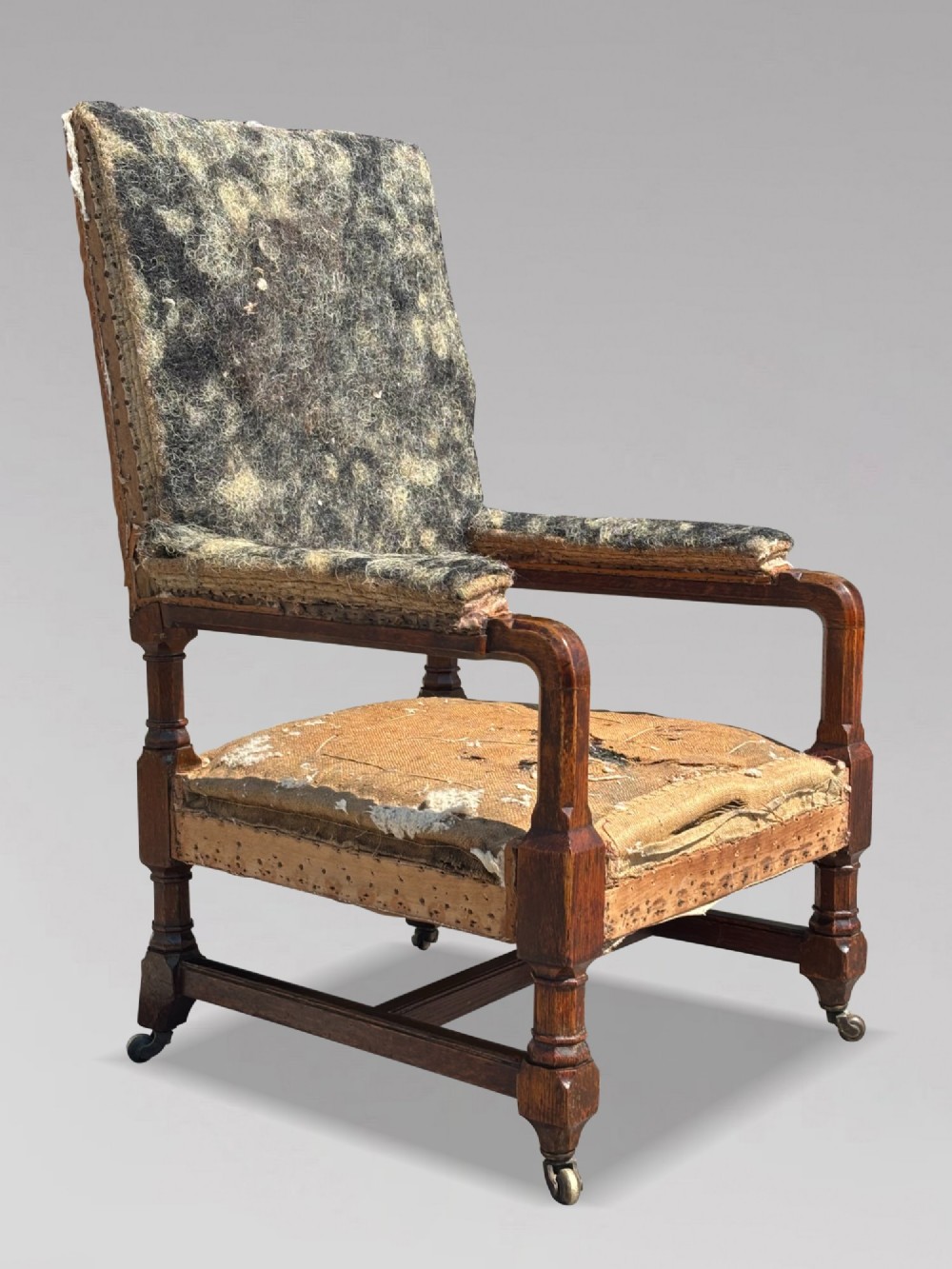 A pair of 19th-century Victorian oak Gothic Revival open armchairs featuring carved timber frames, turned legs with brass castors, and exposed upholstery padding. View VI
