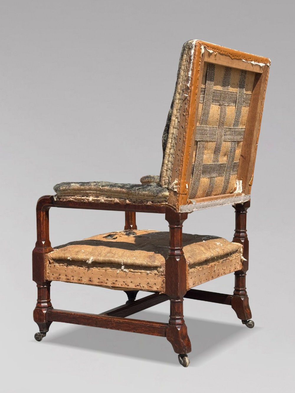 A pair of 19th-century Victorian oak Gothic Revival open armchairs featuring carved timber frames, turned legs with brass castors, and exposed upholstery padding. View VII