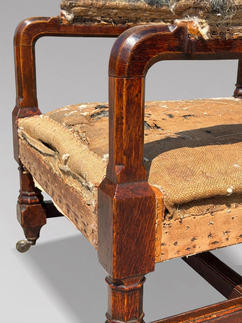 A pair of 19th-century Victorian oak Gothic Revival open armchairs featuring carved timber frames, turned legs with brass castors, and exposed upholstery padding. View VIII