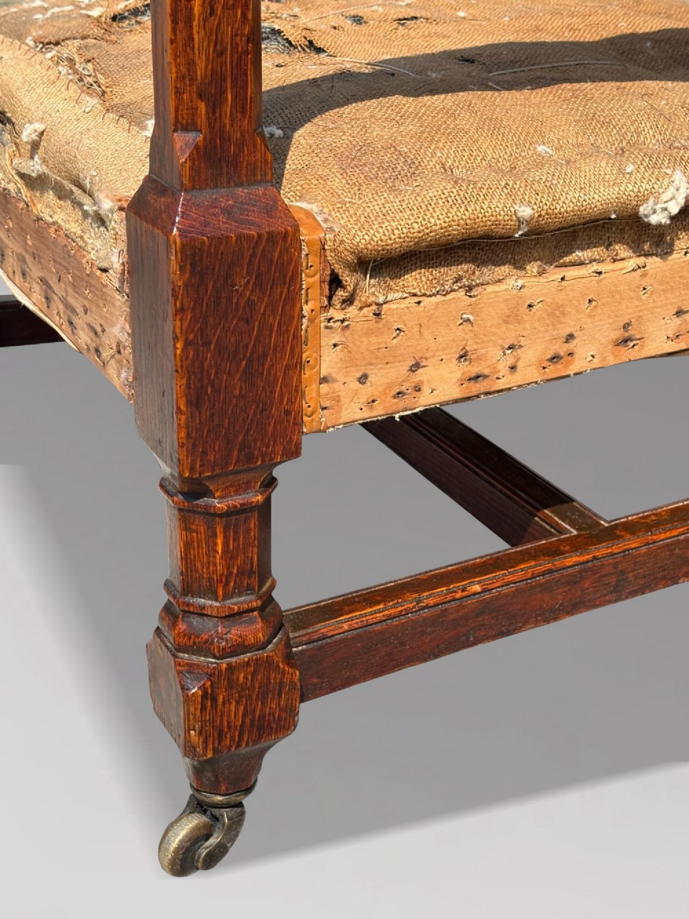A pair of 19th-century Victorian oak Gothic Revival open armchairs featuring carved timber frames, turned legs with brass castors, and exposed upholstery padding. View IX