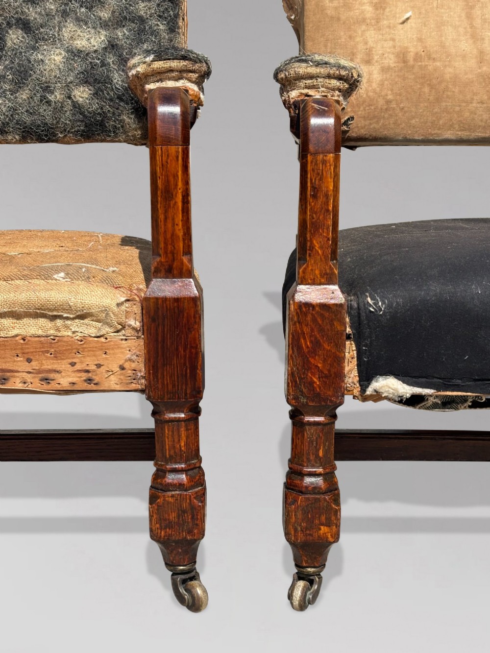 A pair of 19th-century Victorian oak Gothic Revival open armchairs featuring carved timber frames, turned legs with brass castors, and exposed upholstery padding. View XI