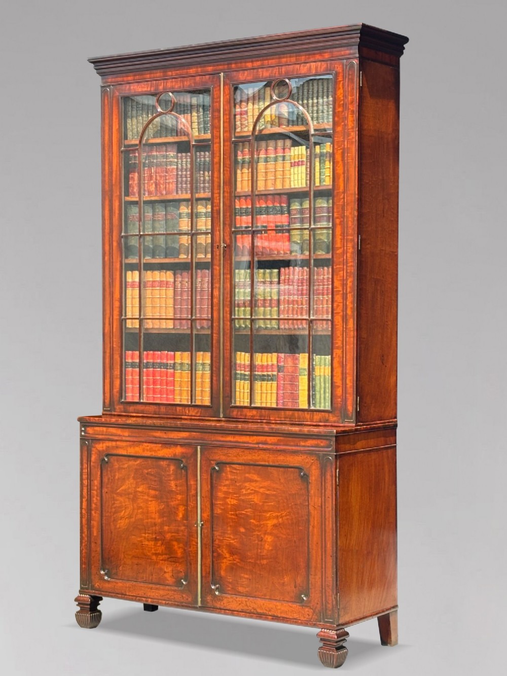 An eighteenth-century George III tall mahogany bookcase featuring two upper astragal glazed doors, lower flame-veneered cabinet doors, and a moulded cornice.