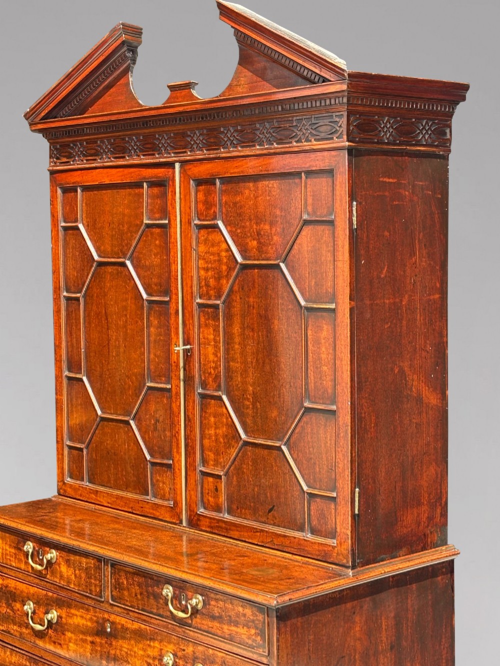 An 18th-century George III mahogany bookcase on chest featuring a broken pediment, carved frieze, geometric astragal glazed doors, and four lower drawers with brass handles. View III