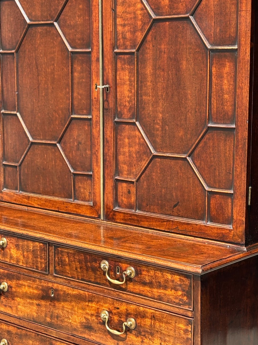 An 18th-century George III mahogany bookcase on chest featuring a broken pediment, carved frieze, geometric astragal glazed doors, and four lower drawers with brass handles. View IV