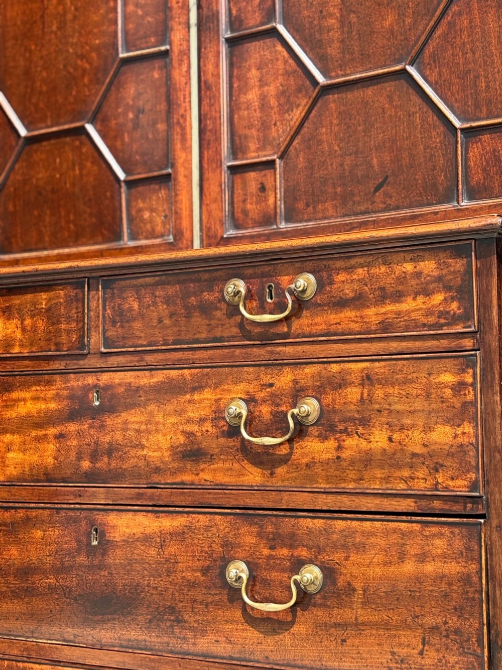 An 18th-century George III mahogany bookcase on chest featuring a broken pediment, carved frieze, geometric astragal glazed doors, and four lower drawers with brass handles. View V
