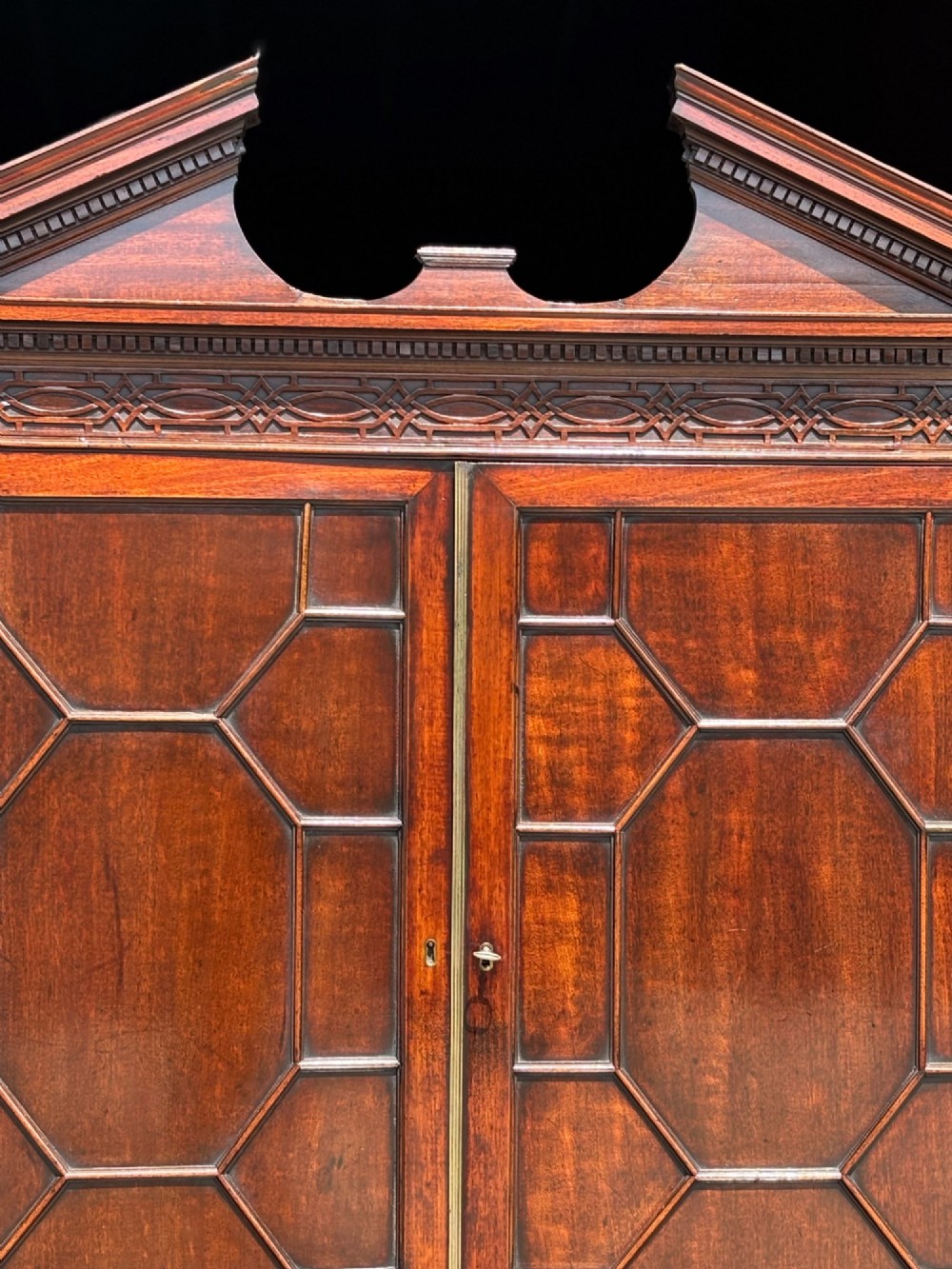 An 18th-century George III mahogany bookcase on chest featuring a broken pediment, carved frieze, geometric astragal glazed doors, and four lower drawers with brass handles. View VI