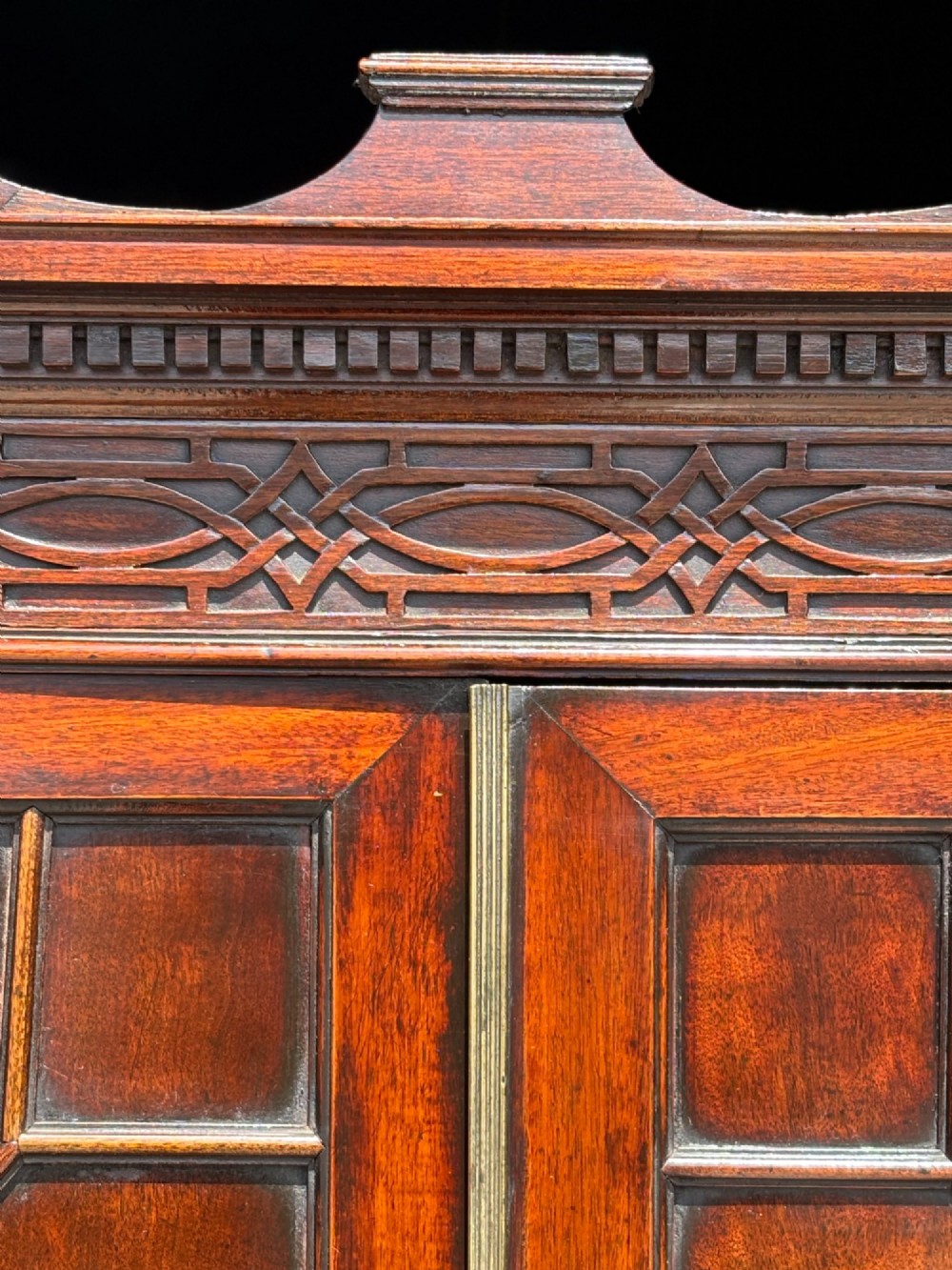 An 18th-century George III mahogany bookcase on chest featuring a broken pediment, carved frieze, geometric astragal glazed doors, and four lower drawers with brass handles. View X