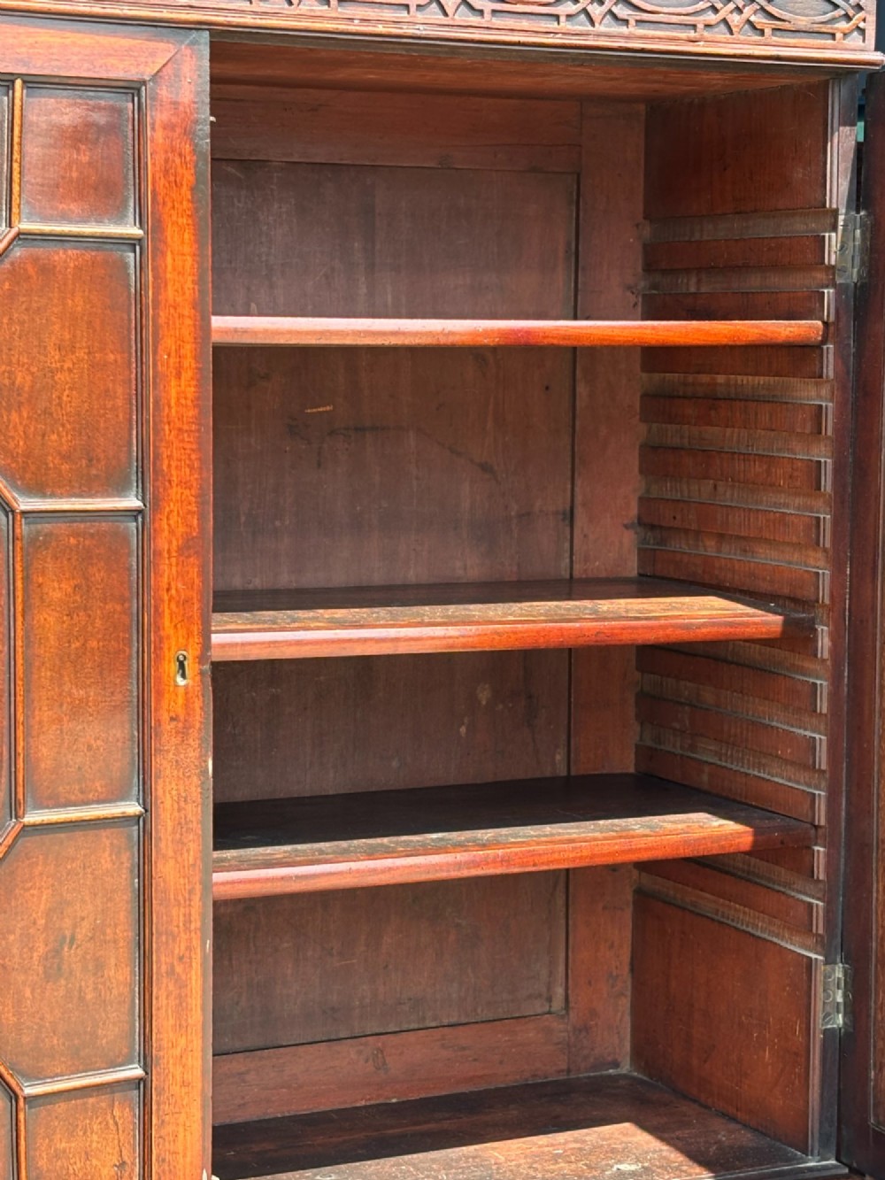 An 18th-century George III mahogany bookcase on chest featuring a broken pediment, carved frieze, geometric astragal glazed doors, and four lower drawers with brass handles. View XI