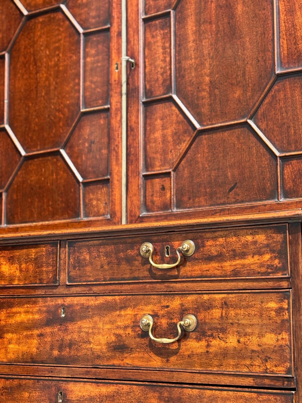 An 18th-century George III mahogany bookcase on chest featuring a broken pediment, carved frieze, geometric astragal glazed doors, and four lower drawers with brass handles. View XII