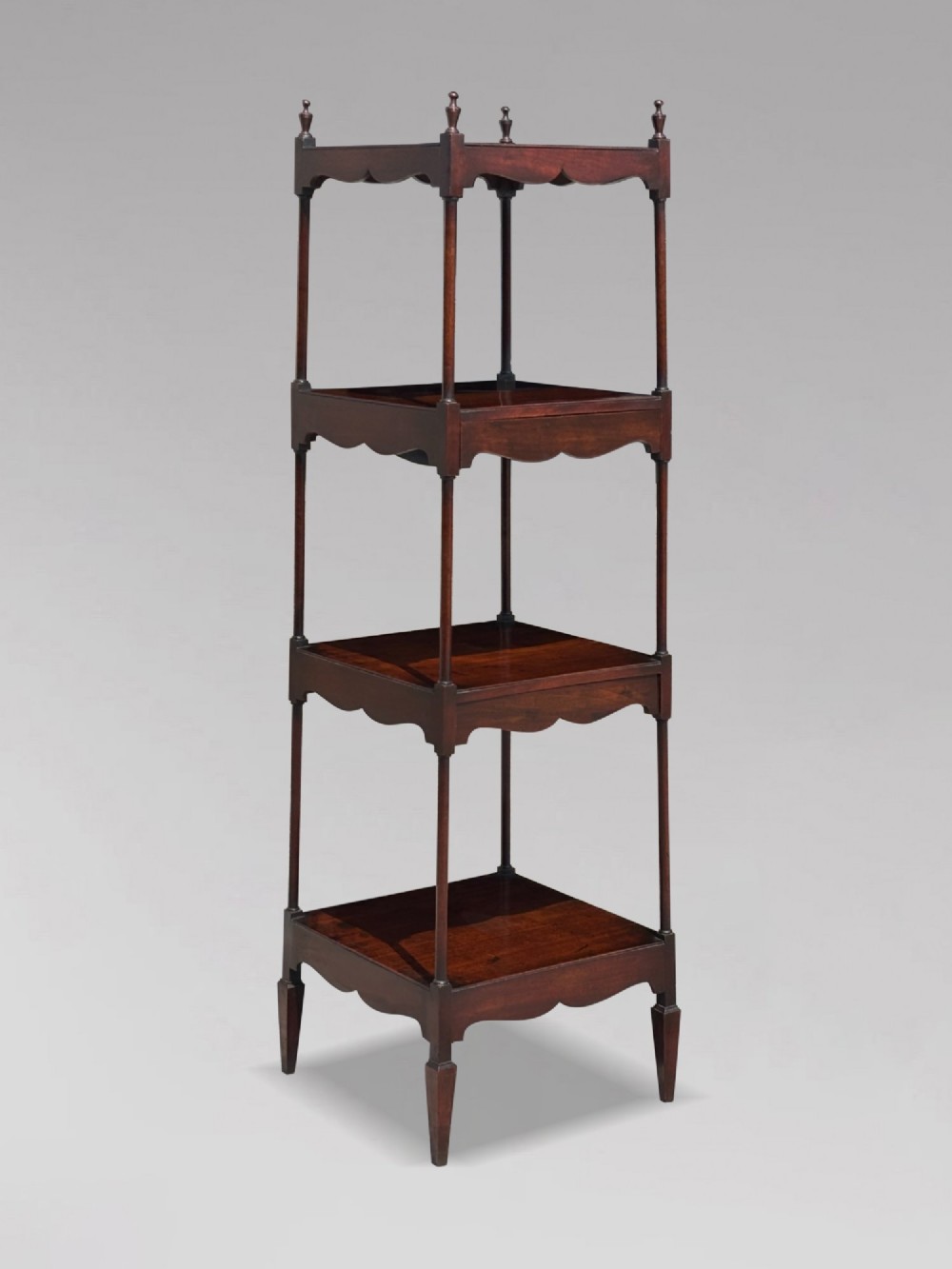 A four-tiered George III mahogany whatnot featuring slender corner supports, turned finials, scalloped aprons, and square tapered legs.