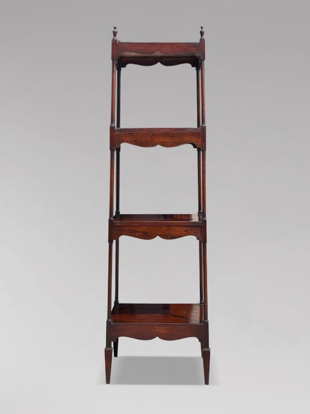 A four-tiered George III mahogany whatnot featuring slender corner supports, turned finials, scalloped aprons, and square tapered legs. View II