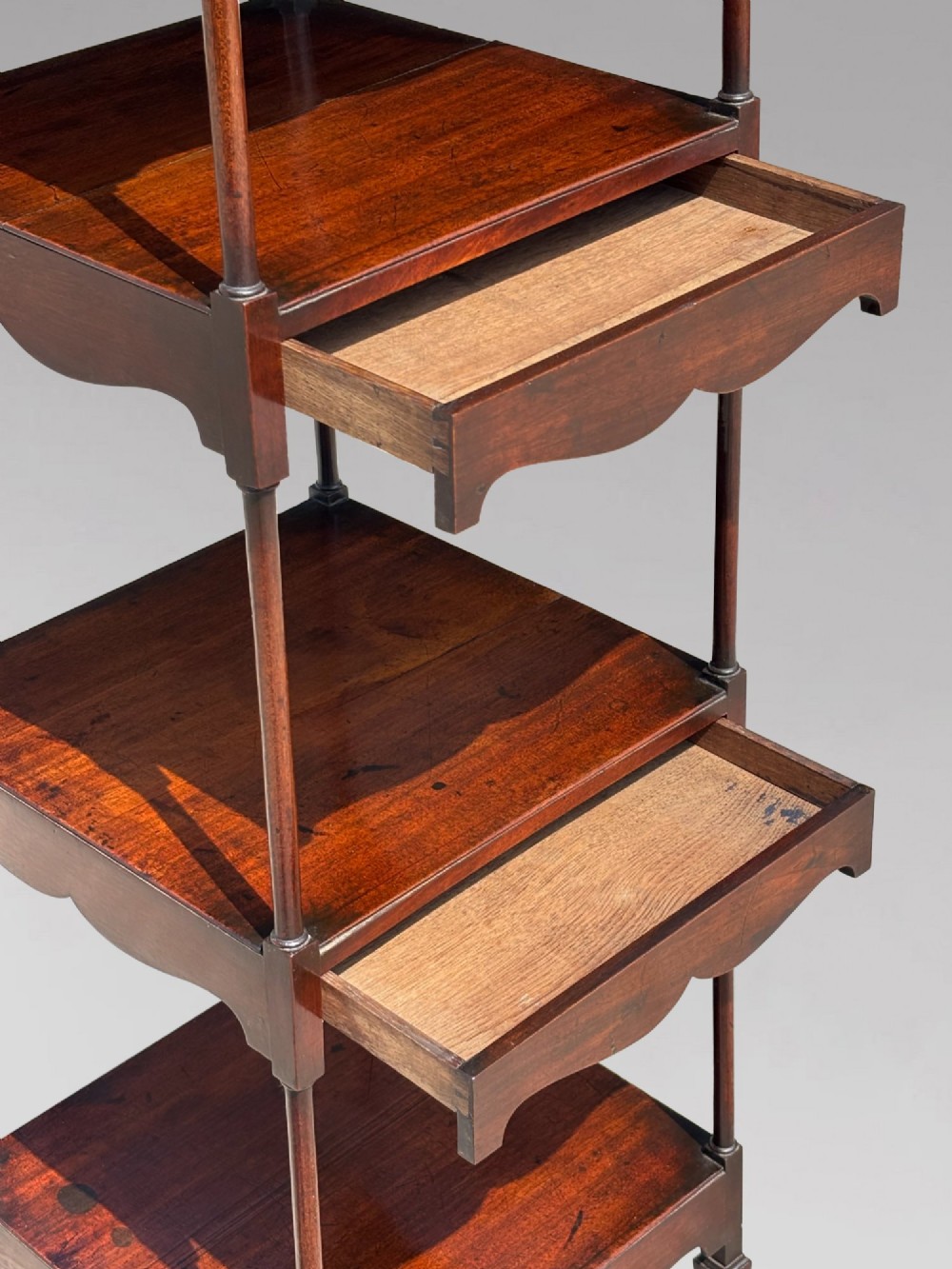 A four-tiered George III mahogany whatnot featuring slender corner supports, turned finials, scalloped aprons, and square tapered legs. View IV