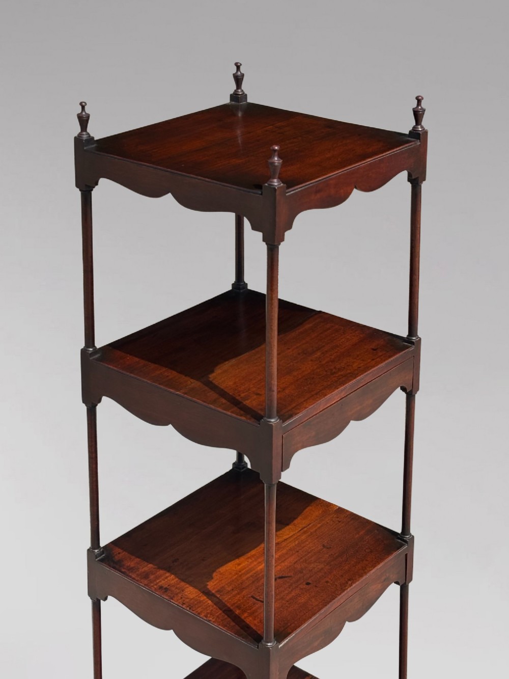 A four-tiered George III mahogany whatnot featuring slender corner supports, turned finials, scalloped aprons, and square tapered legs. View V