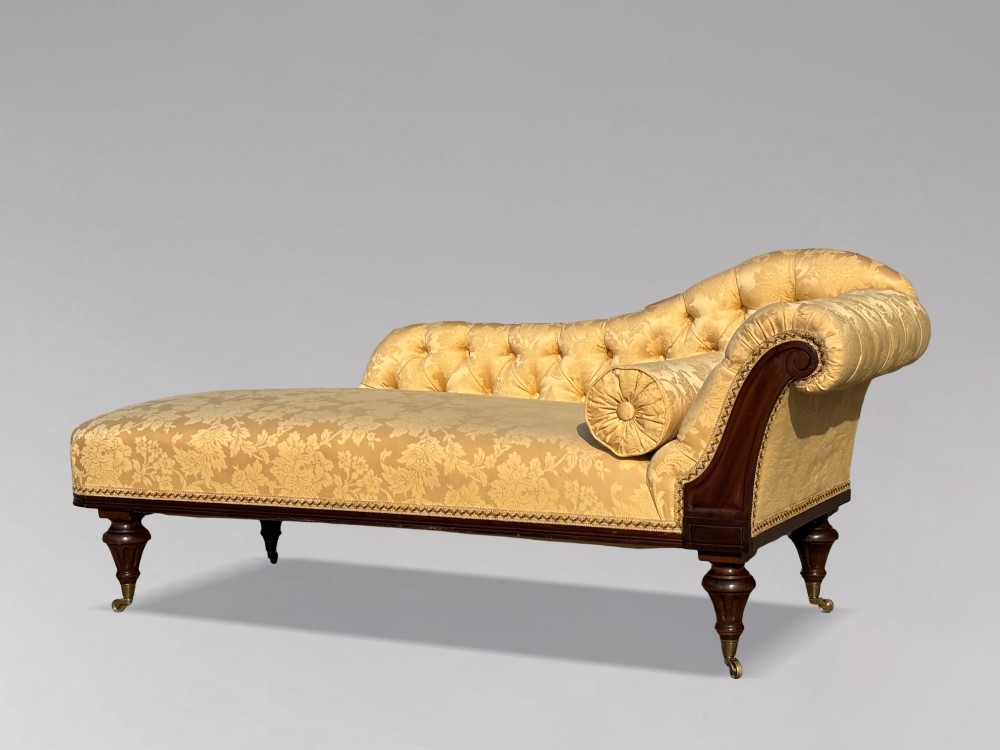 A 19th-century Regency mahogany chaise longue upholstered in yellow damask fabric with deep buttoning, a bolster cushion, and turned legs on brass castors.