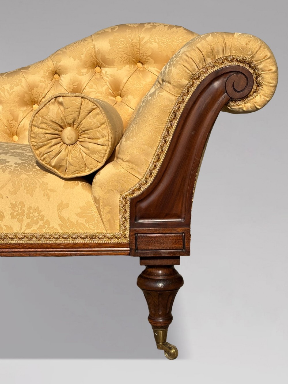 A 19th-century Regency mahogany chaise longue upholstered in yellow damask fabric with deep buttoning, a bolster cushion, and turned legs on brass castors. View IV