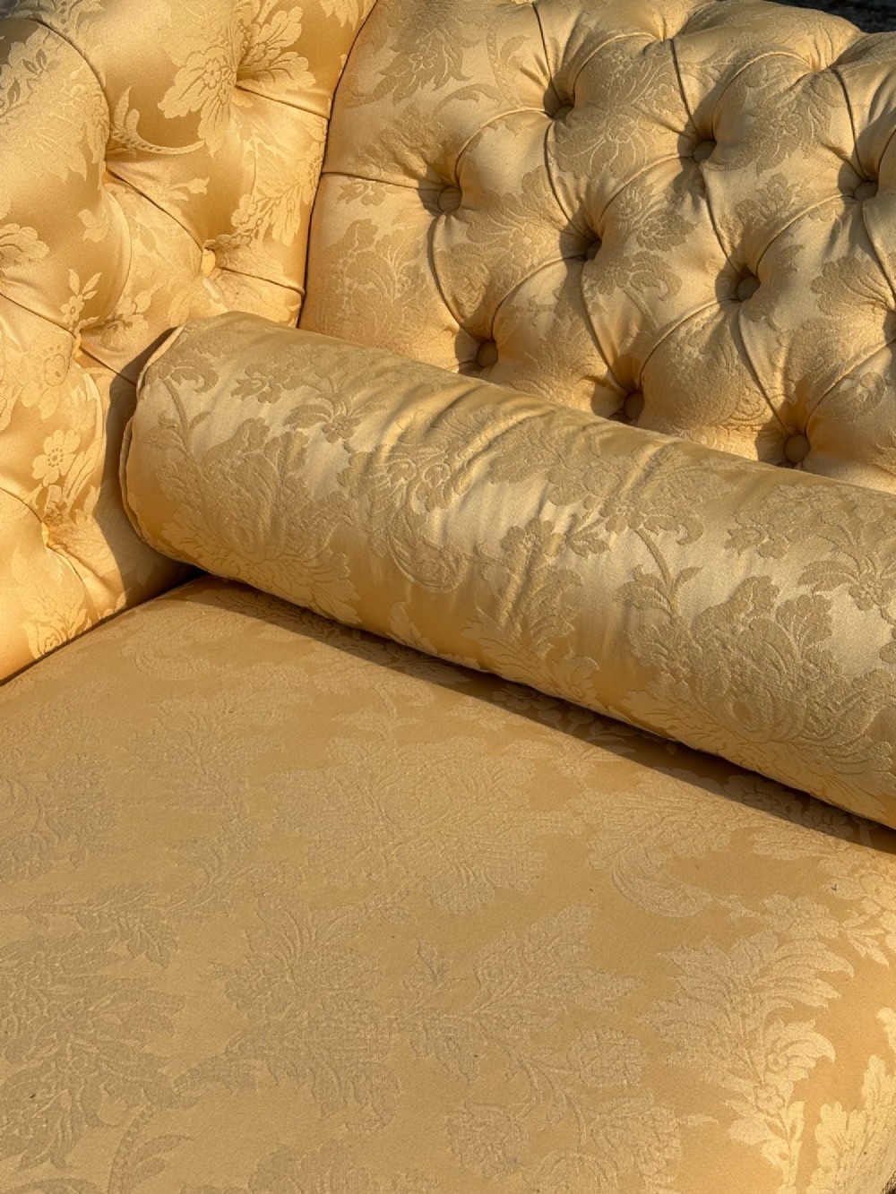 A 19th-century Regency mahogany chaise longue upholstered in yellow damask fabric with deep buttoning, a bolster cushion, and turned legs on brass castors. View V