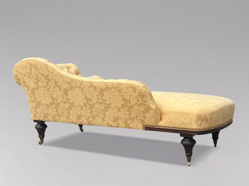 A 19th-century Regency mahogany chaise longue upholstered in yellow damask fabric with deep buttoning, a bolster cushion, and turned legs on brass castors. View X