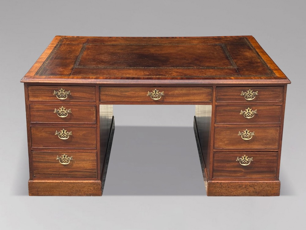 An 18th-century George III mahogany partners desk featuring an inset leather writing surface, brass swan-neck handles, and twin pedestals with stacked drawers.