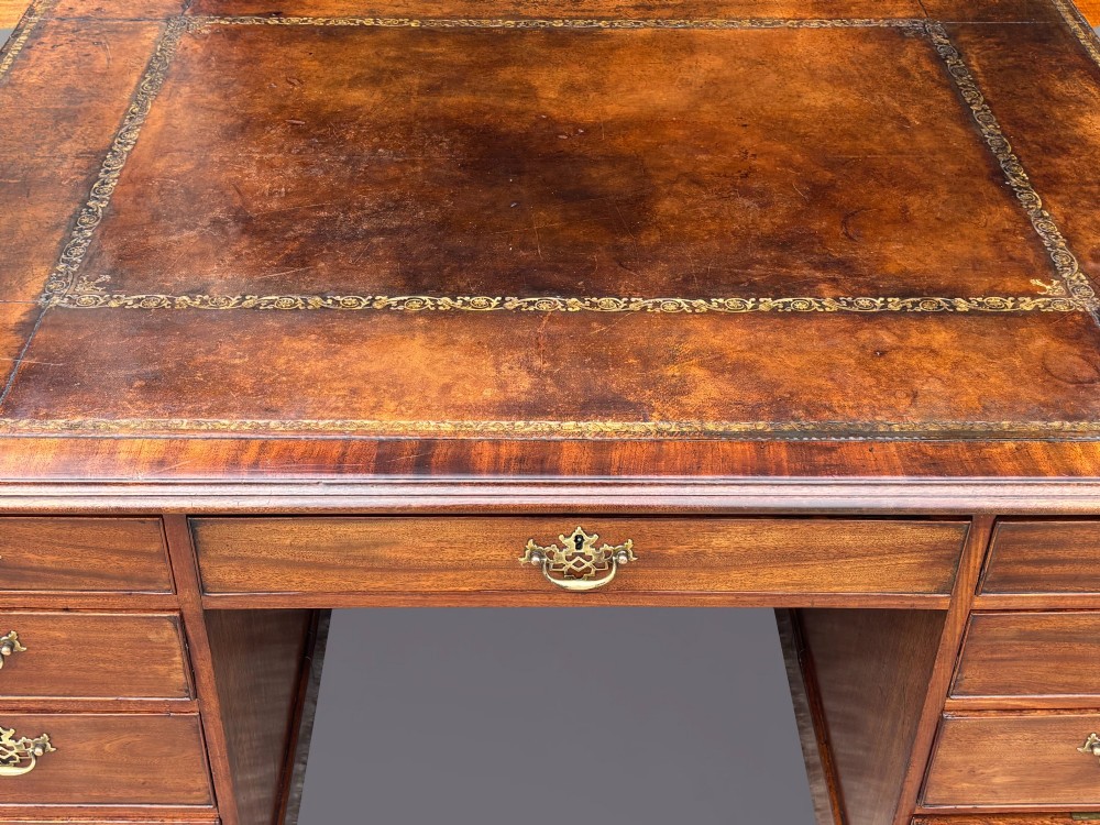 An 18th-century George III mahogany partners desk featuring an inset leather writing surface, brass swan-neck handles, and twin pedestals with stacked drawers. View V