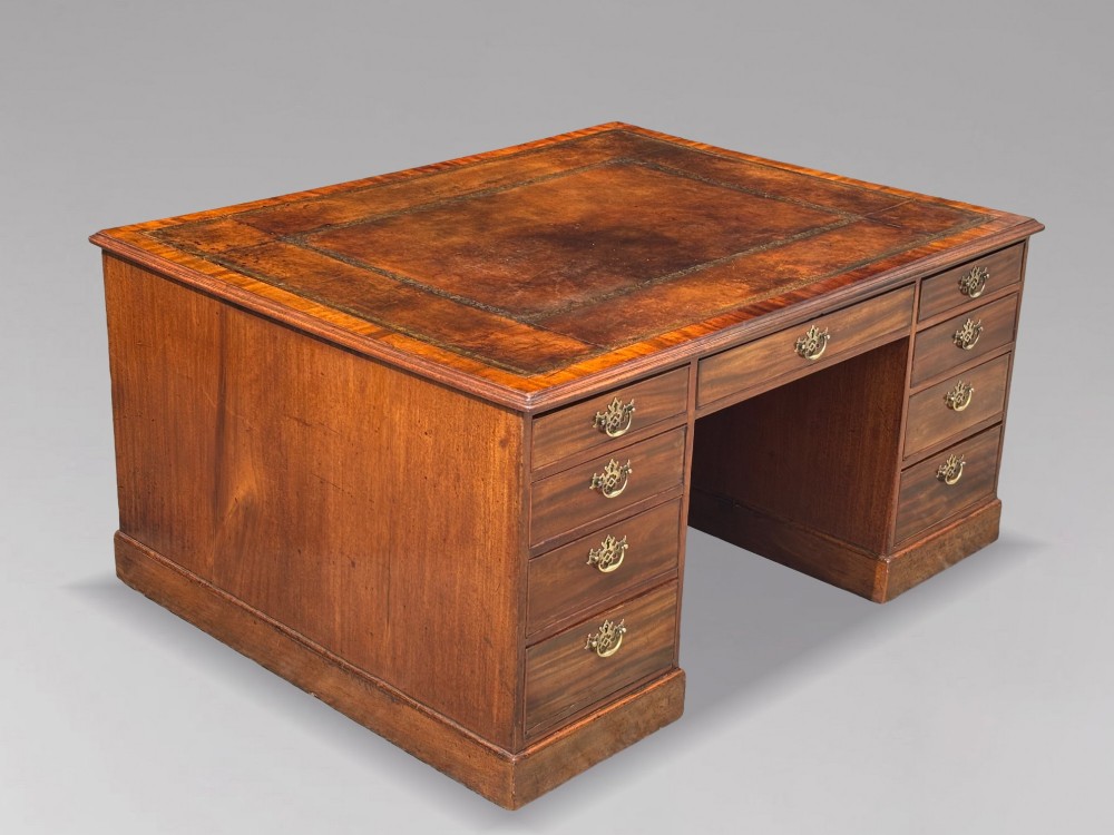 An 18th-century George III mahogany partners desk featuring an inset leather writing surface, brass swan-neck handles, and twin pedestals with stacked drawers. View IX