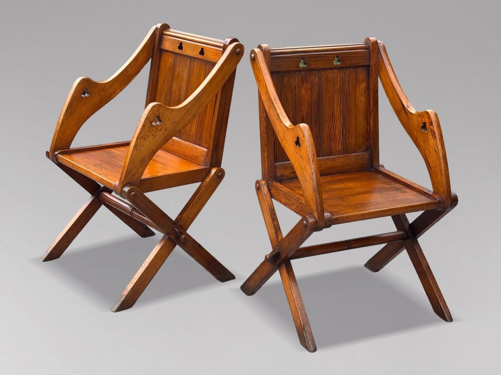 A pair of Victorian pitch pine Glastonbury armchairs featuring sloped armrests, X-frame bases, and pierced trefoil motifs on the back panels. View II