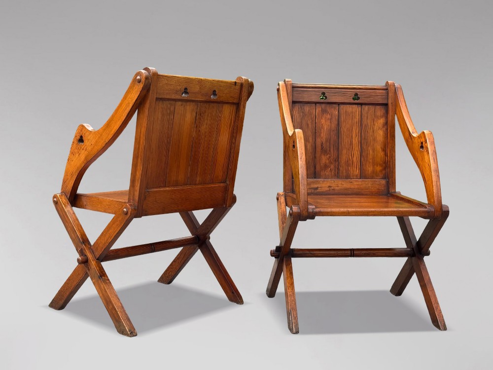 A pair of Victorian pitch pine Glastonbury armchairs featuring sloped armrests, X-frame bases, and pierced trefoil motifs on the back panels. View XI