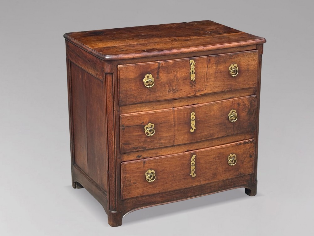 A 17th-century French Provincial walnut commode featuring three long drawers decorated with brass drop handles and central escutcheons.