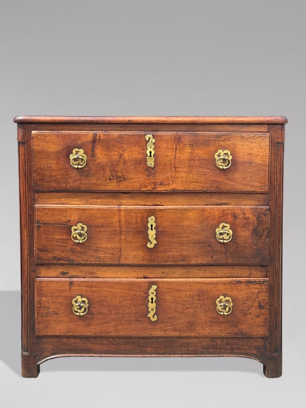 A 17th-century French Provincial walnut commode featuring three long drawers decorated with brass drop handles and central escutcheons. View IX
