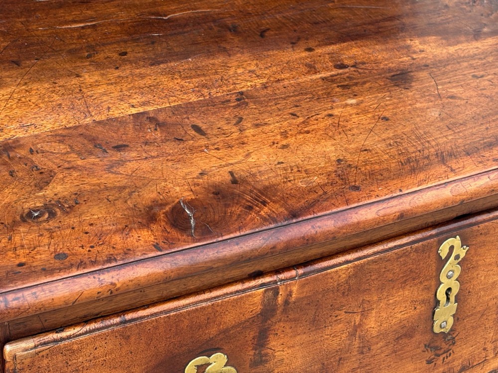 A 17th-century French Provincial walnut commode featuring three long drawers decorated with brass drop handles and central escutcheons. View X