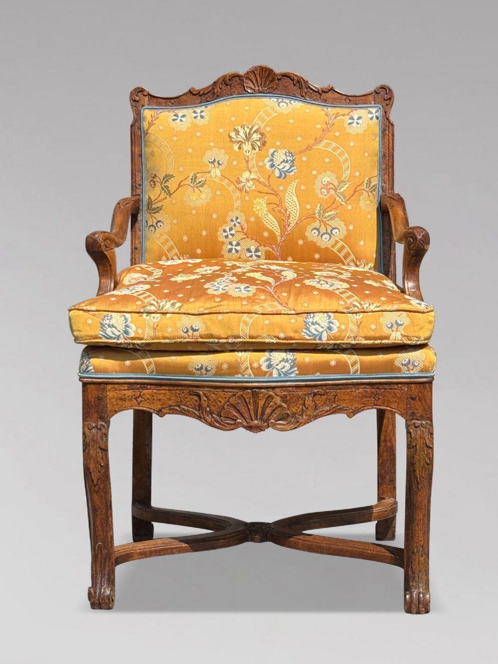 An 18th-century French carved walnut armchair with cabriole legs, an X-form stretcher, and yellow floral upholstered cushions finished with blue trim. View II