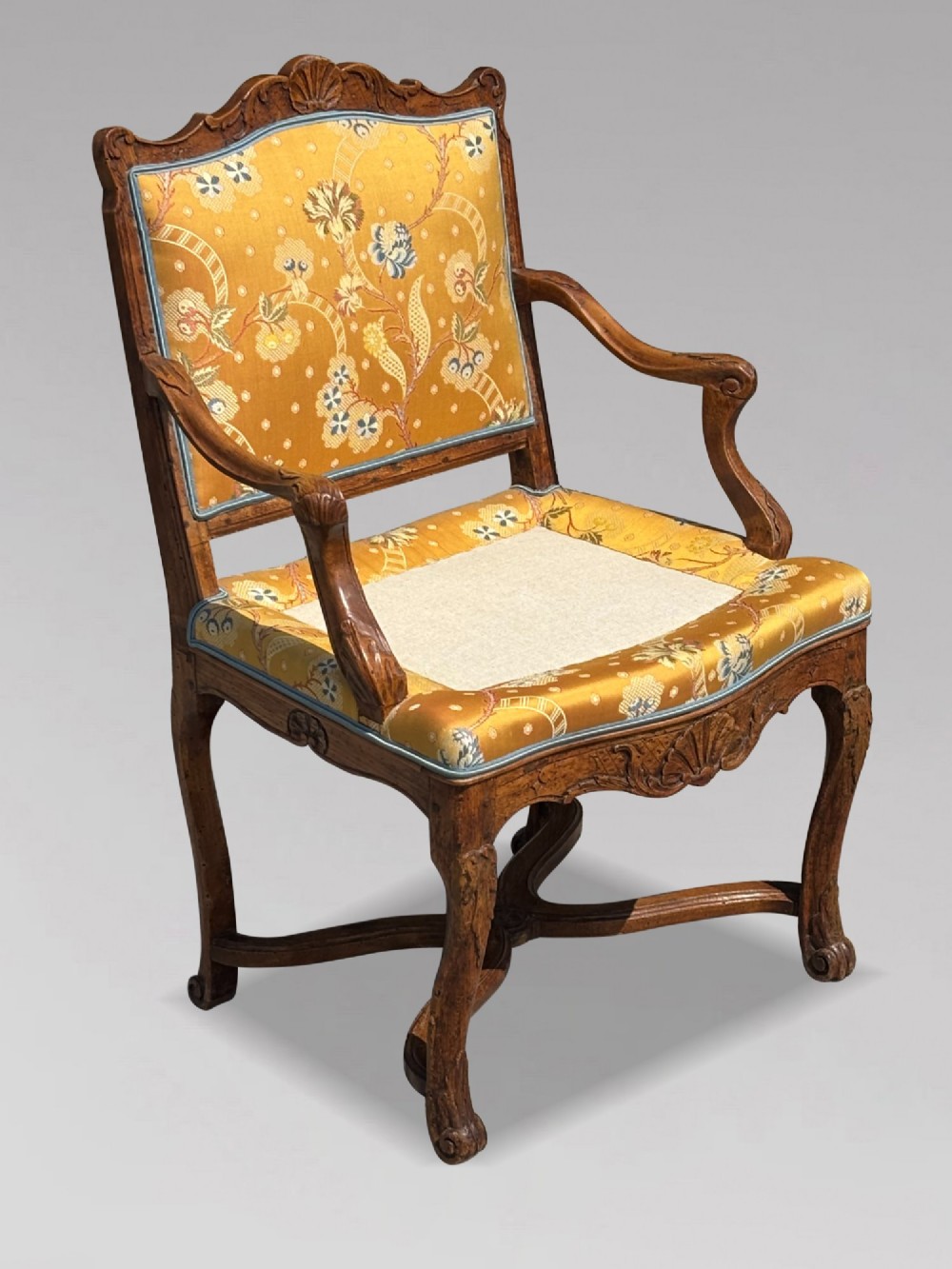 An 18th-century French carved walnut armchair with cabriole legs, an X-form stretcher, and yellow floral upholstered cushions finished with blue trim. View V