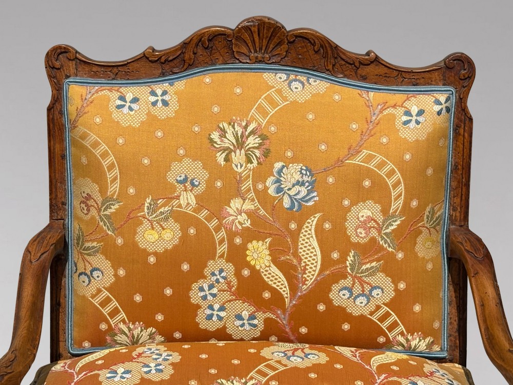 An 18th-century French carved walnut armchair with cabriole legs, an X-form stretcher, and yellow floral upholstered cushions finished with blue trim. View VI