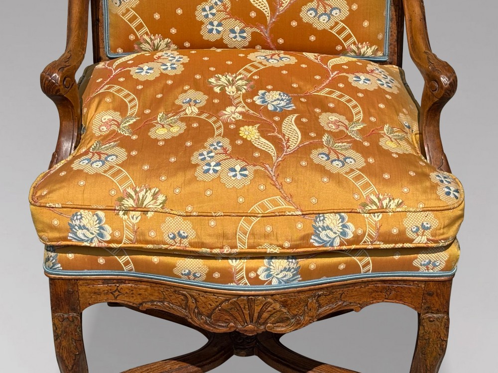 An 18th-century French carved walnut armchair with cabriole legs, an X-form stretcher, and yellow floral upholstered cushions finished with blue trim. View VII