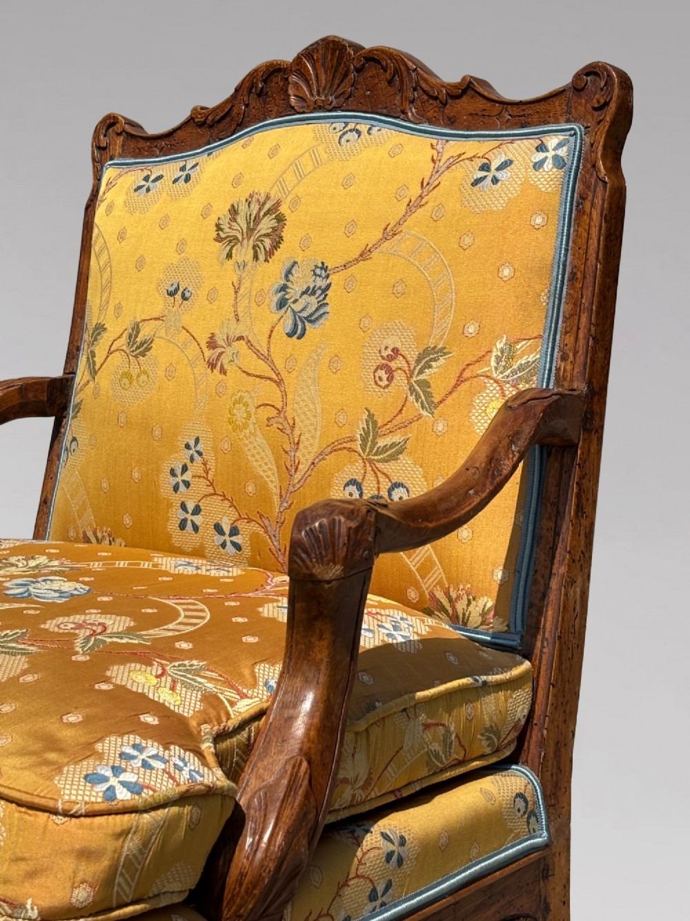 An 18th-century French carved walnut armchair with cabriole legs, an X-form stretcher, and yellow floral upholstered cushions finished with blue trim. View IX