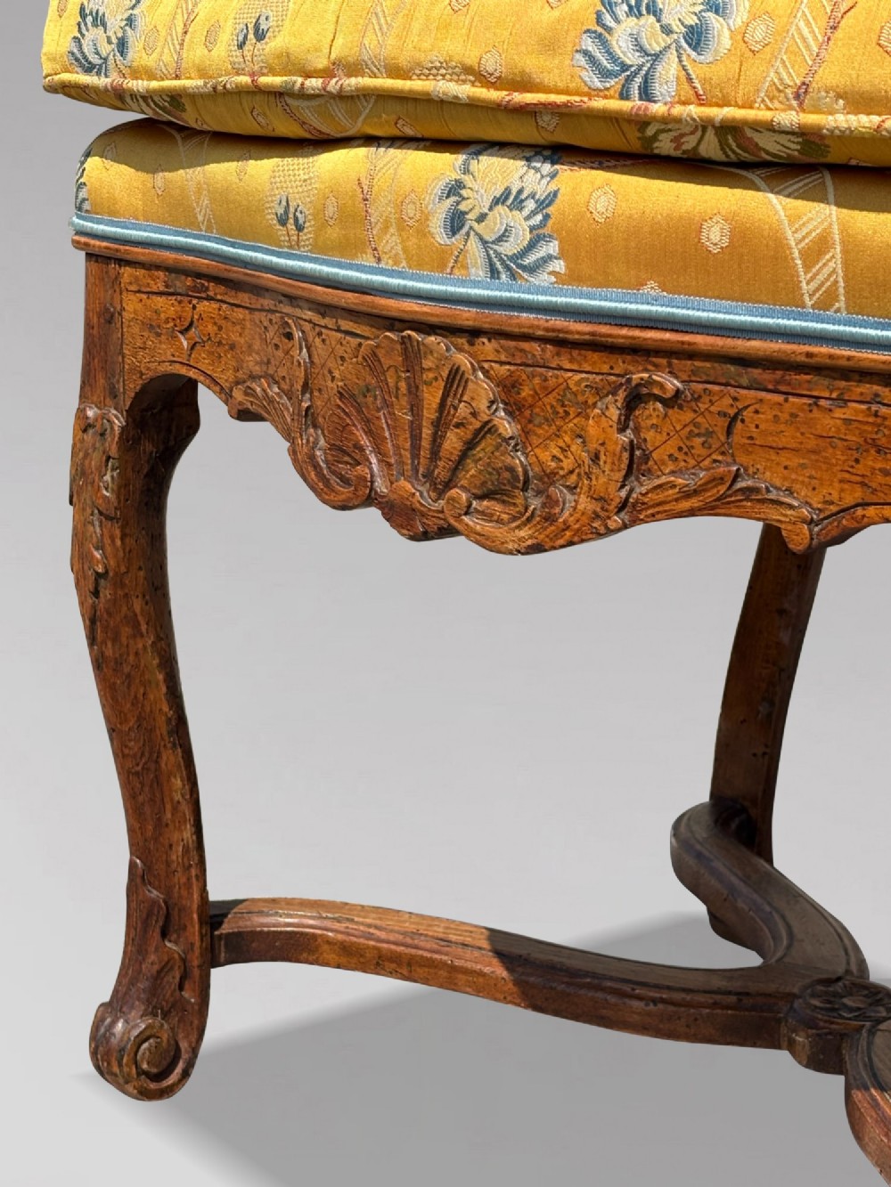 An 18th-century French carved walnut armchair with cabriole legs, an X-form stretcher, and yellow floral upholstered cushions finished with blue trim. View XI