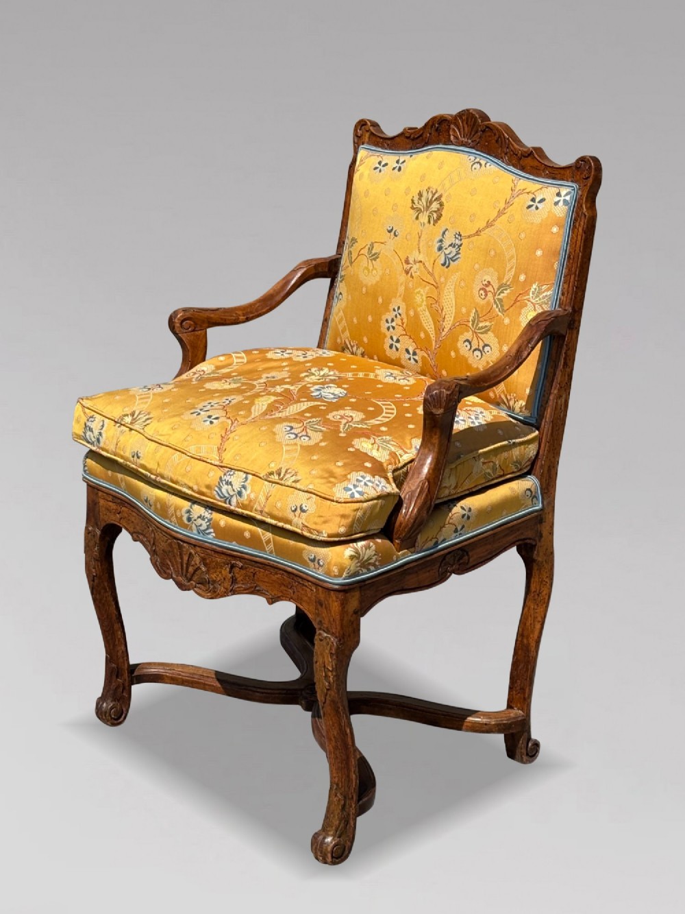 An 18th-century French carved walnut armchair with cabriole legs, an X-form stretcher, and yellow floral upholstered cushions finished with blue trim. View XII