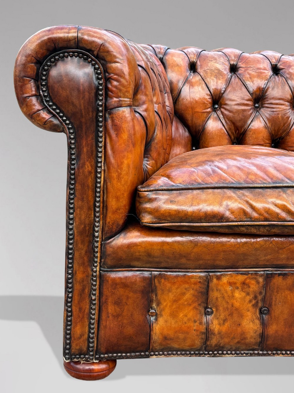 A Victorian three-seater Chesterfield sofa with brown deep-buttoned leather, three seat cushions, brass stud trim, and turned feet. View V