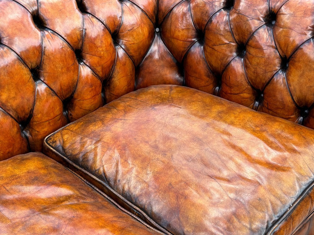 A Victorian three-seater Chesterfield sofa with brown deep-buttoned leather, three seat cushions, brass stud trim, and turned feet. View VI