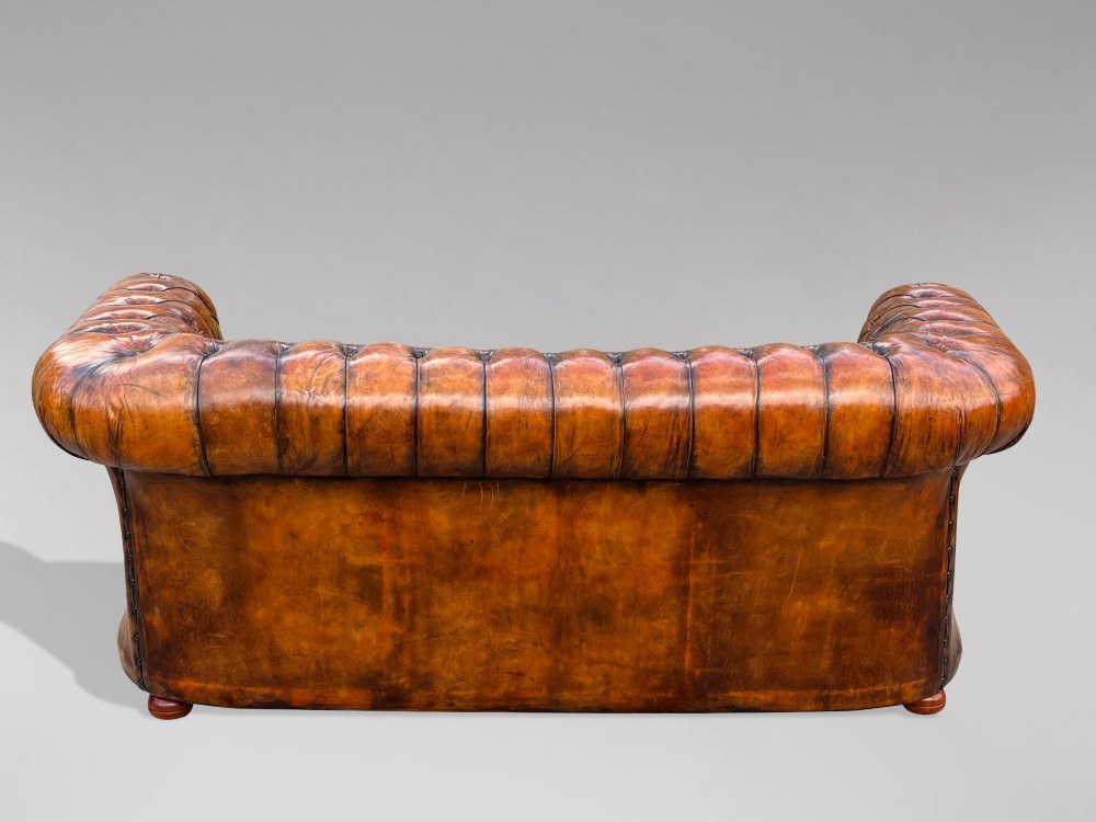 A Victorian three-seater Chesterfield sofa with brown deep-buttoned leather, three seat cushions, brass stud trim, and turned feet. View VII
