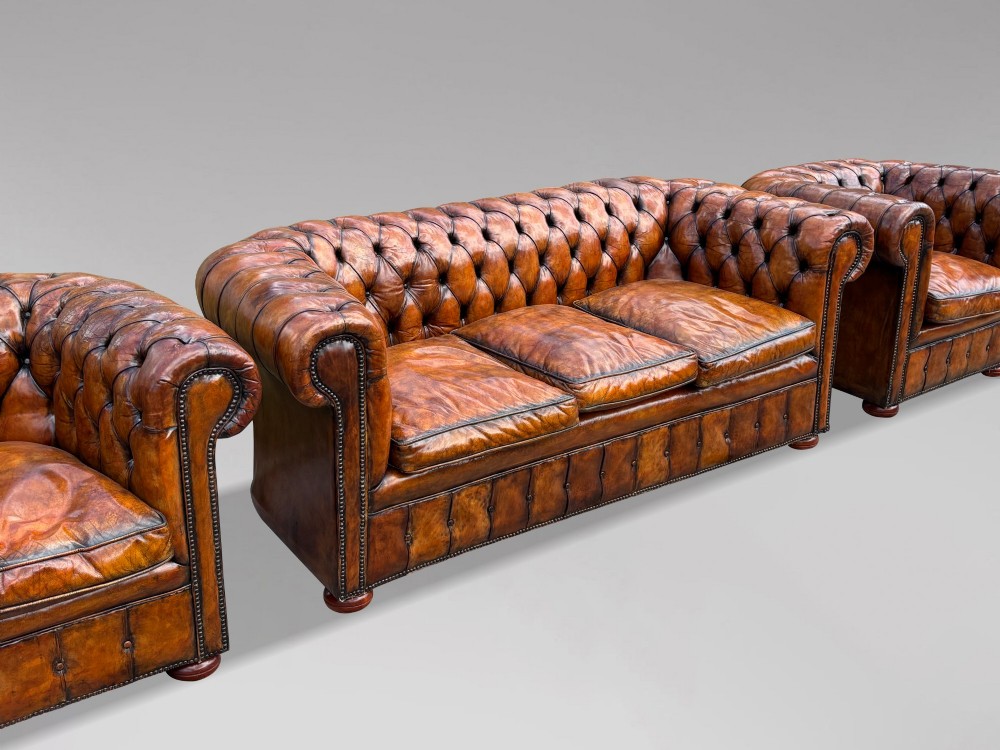 A Victorian three-seater Chesterfield sofa with brown deep-buttoned leather, three seat cushions, brass stud trim, and turned feet. View IX