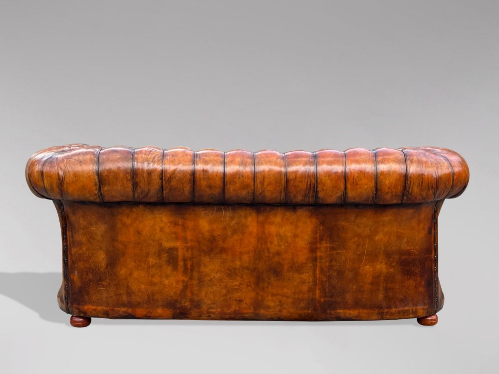 A Victorian three-seater Chesterfield sofa with brown deep-buttoned leather, three seat cushions, brass stud trim, and turned feet. View XI