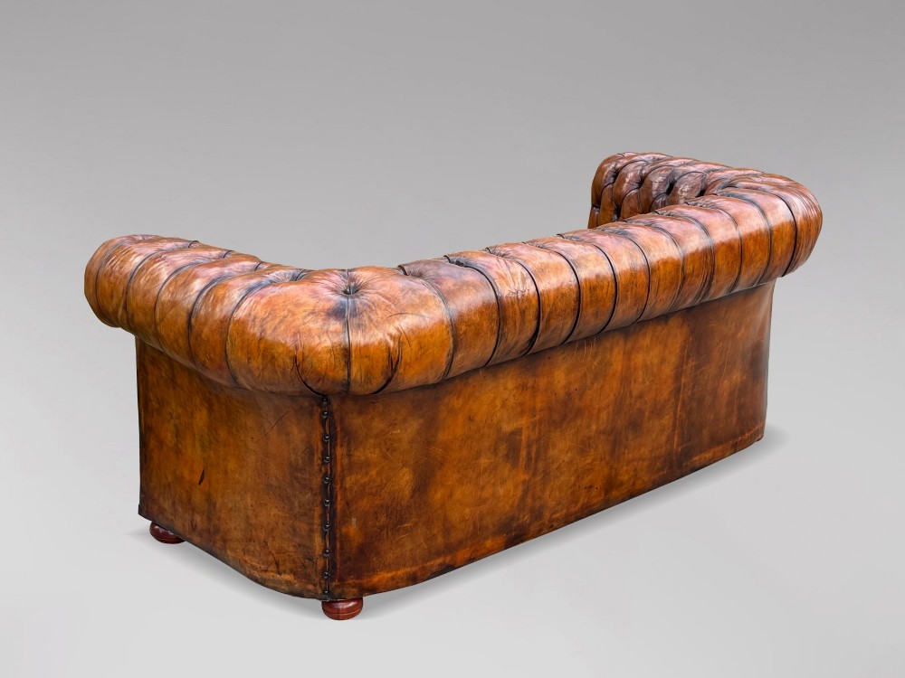 A Victorian three-seater Chesterfield sofa with brown deep-buttoned leather, three seat cushions, brass stud trim, and turned feet. View XII